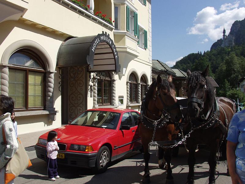 P8056917.jpg - Hotel Muller with our car and L watching the horses.  You can see Neuschwanstein in the background.